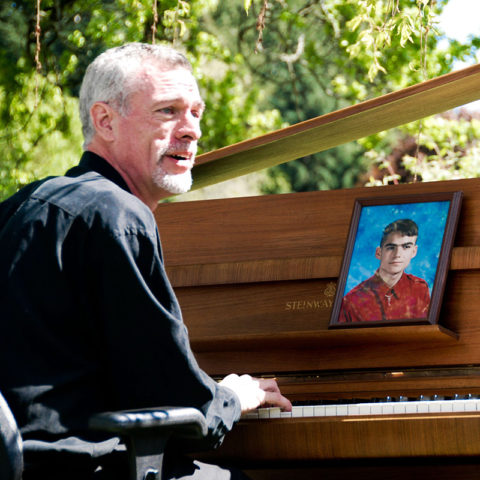 Steve Schalchlin playing John Lennon’s piano. Bill Clayton watches on from the photograph. May 8, 2007, in Olympia, WA. Photo by Caroline True. 